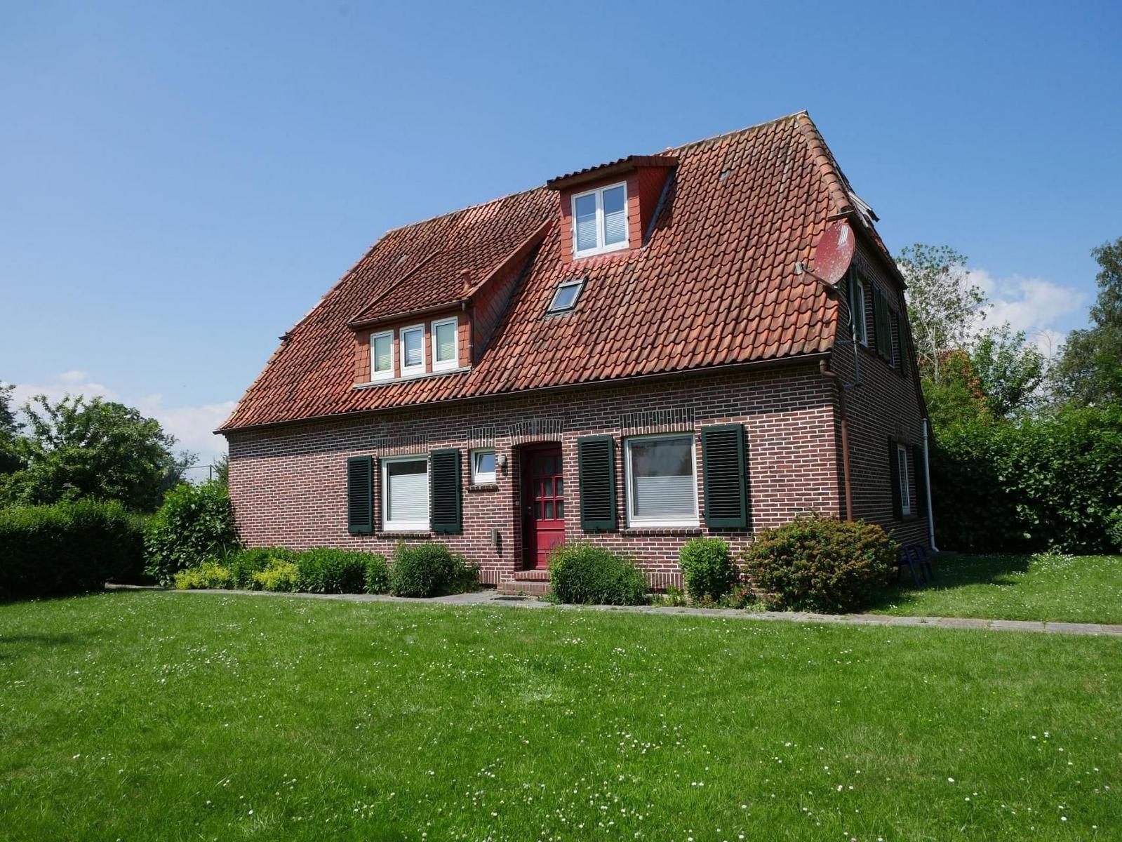 Ein zweistöckiges Haus mit rotem Dach und grüner Umgebung.