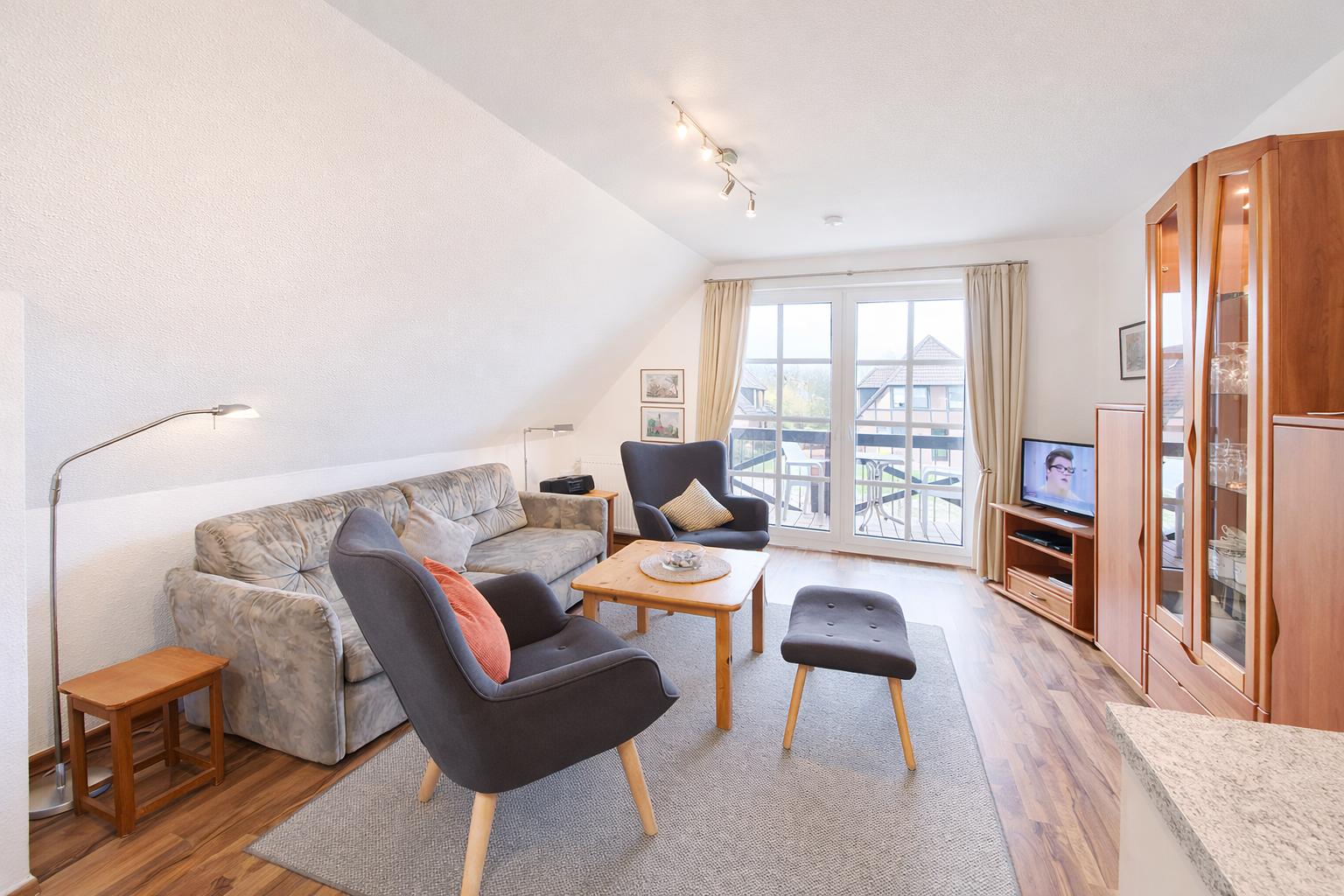 Wohnzimmer mit Sofa, Sessel und TV. Durchgang zur Terrasse mit Blick auf die Umgebung.
