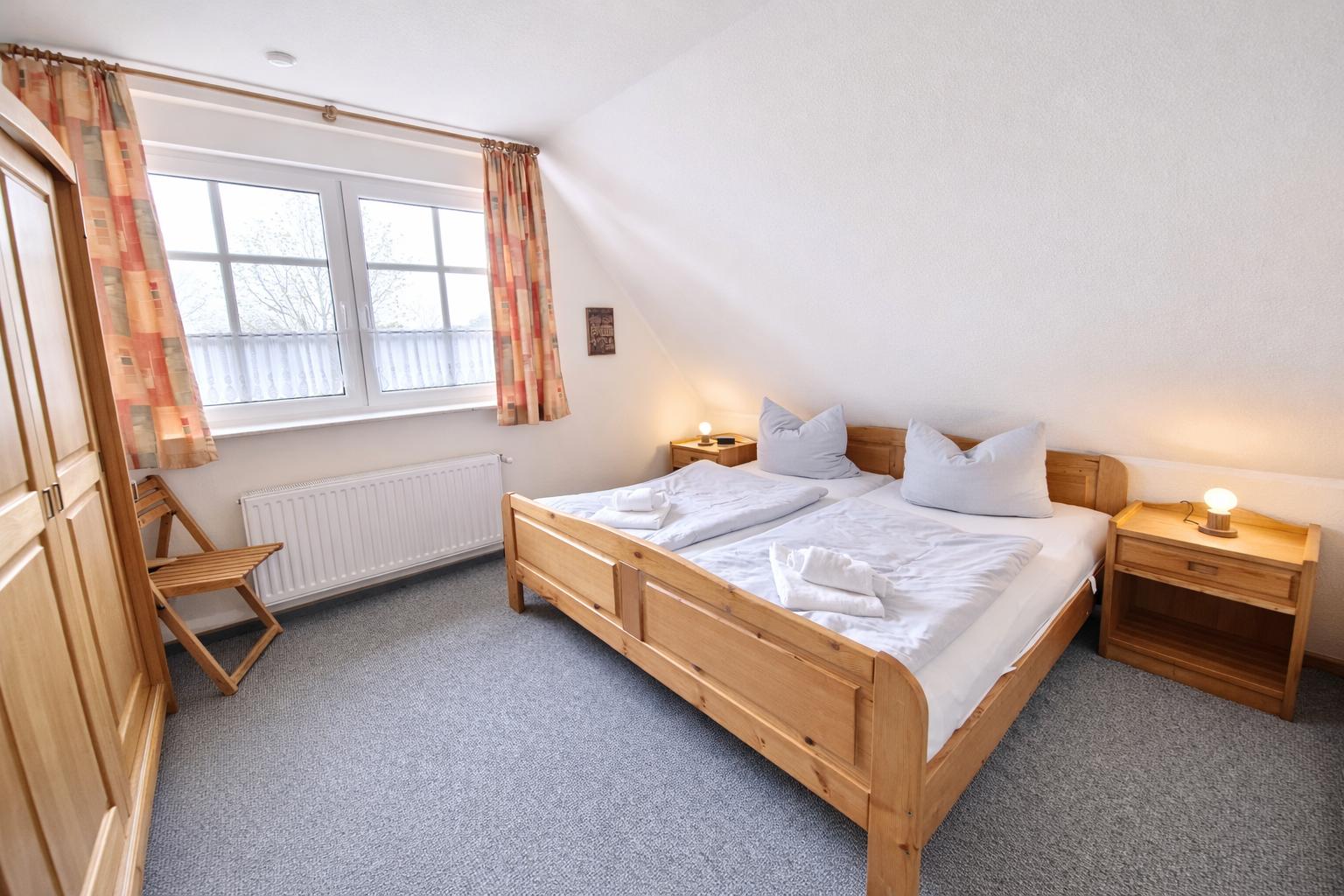 Schlafzimmer mit Holzbett, zwei Nachttischen und Fenster mit Vorhängen.
