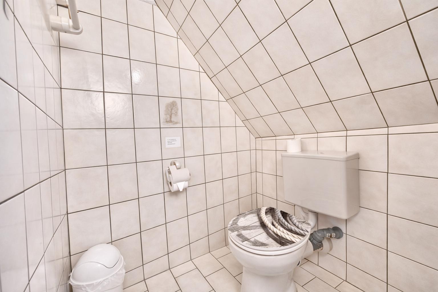 Badezimmer mit Toilette, WC und Abflussrohr. Wände und Boden sind mit Fliesen ausgelegt.