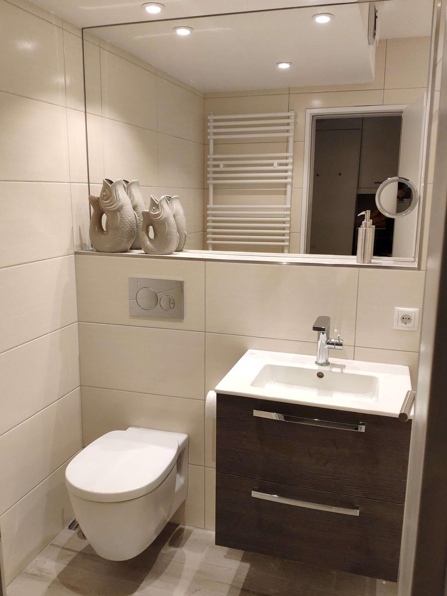 Badezimmer mit Toilette, Waschbecken und Spiegel. Drei Fischfiguren stehen auf dem Waschbecken.