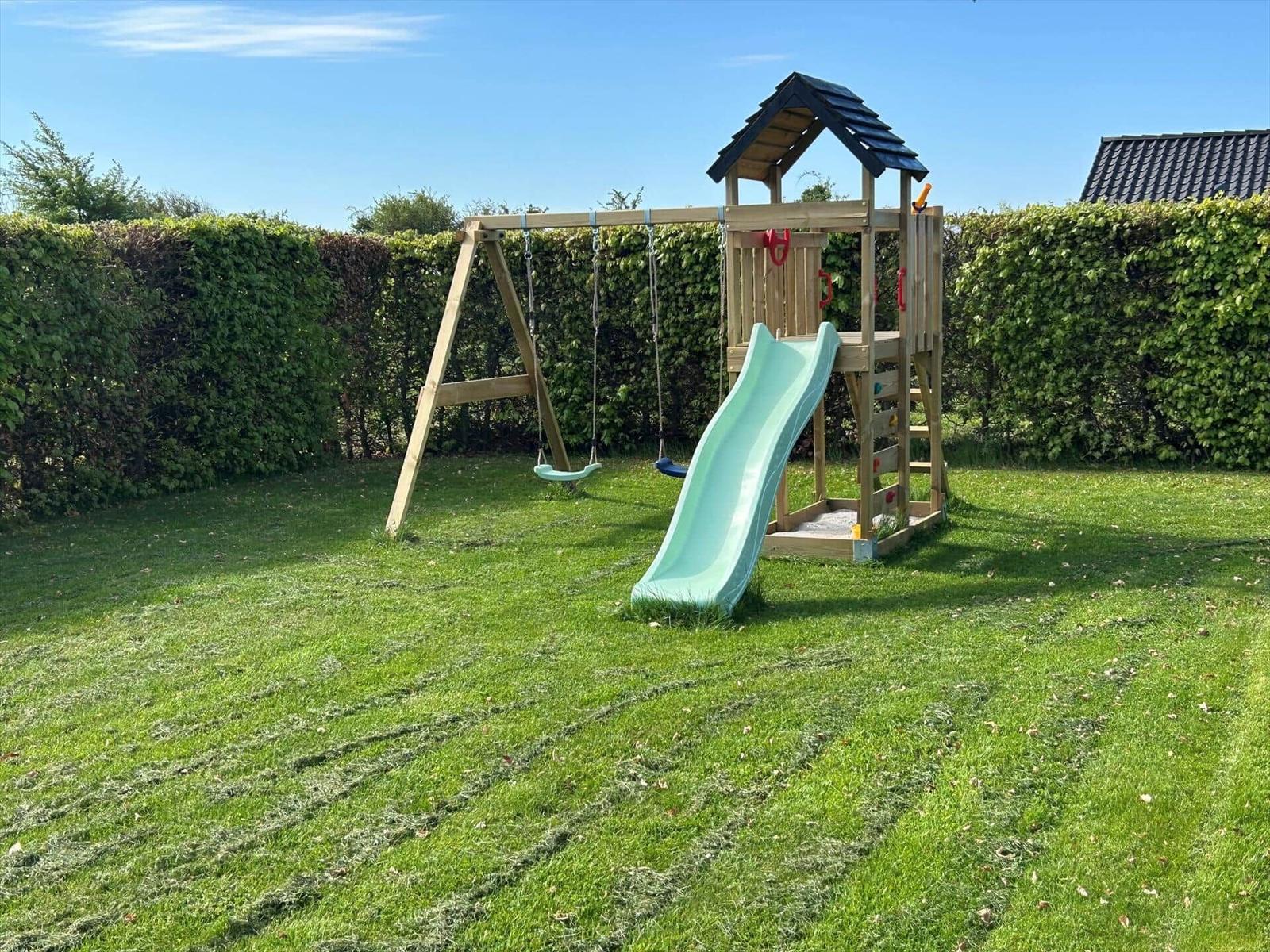 Hinterhof mit Holzspielplatz, Schaukel und Rutsche auf grünem Rasen.