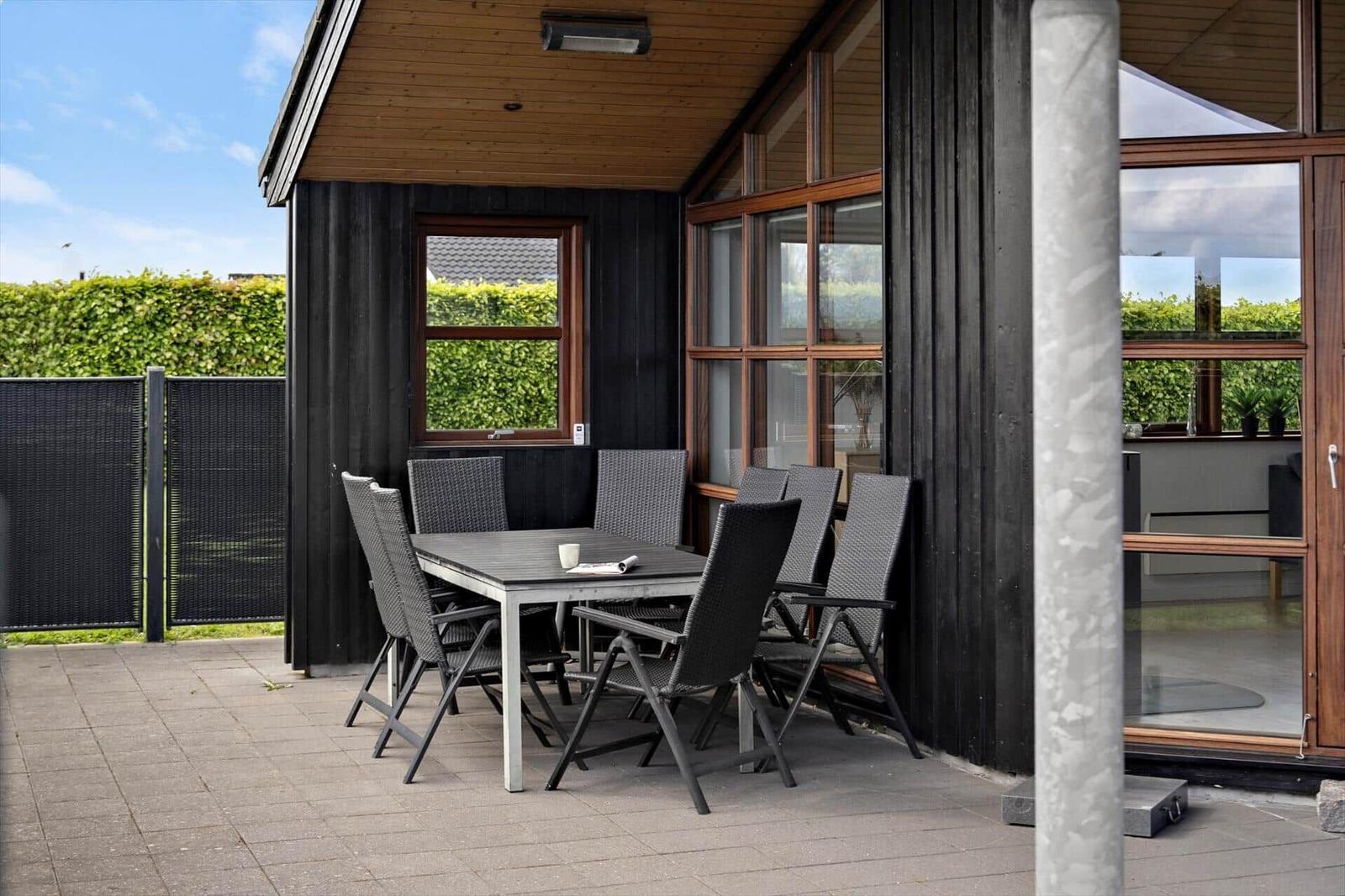 Terrasse mit Tisch und Stühlen vor einem Haus mit großem Fenster.