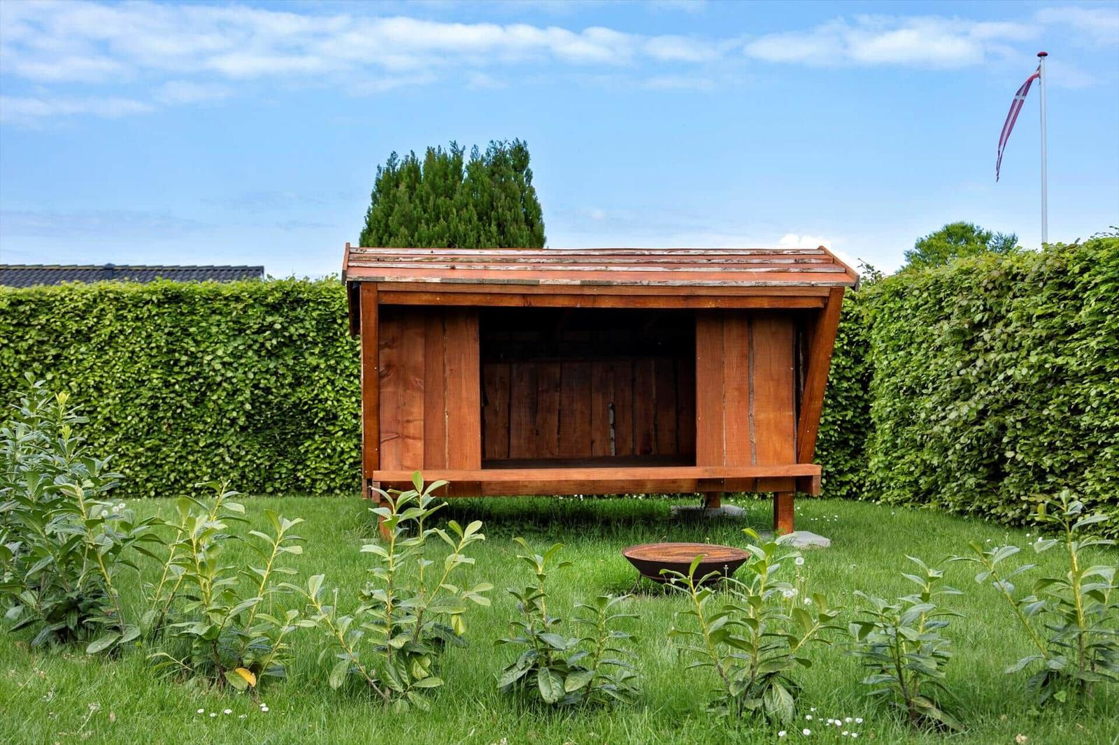 Holzkonstruktion im Garten mit Rasen, Sträuchern und Hecke.