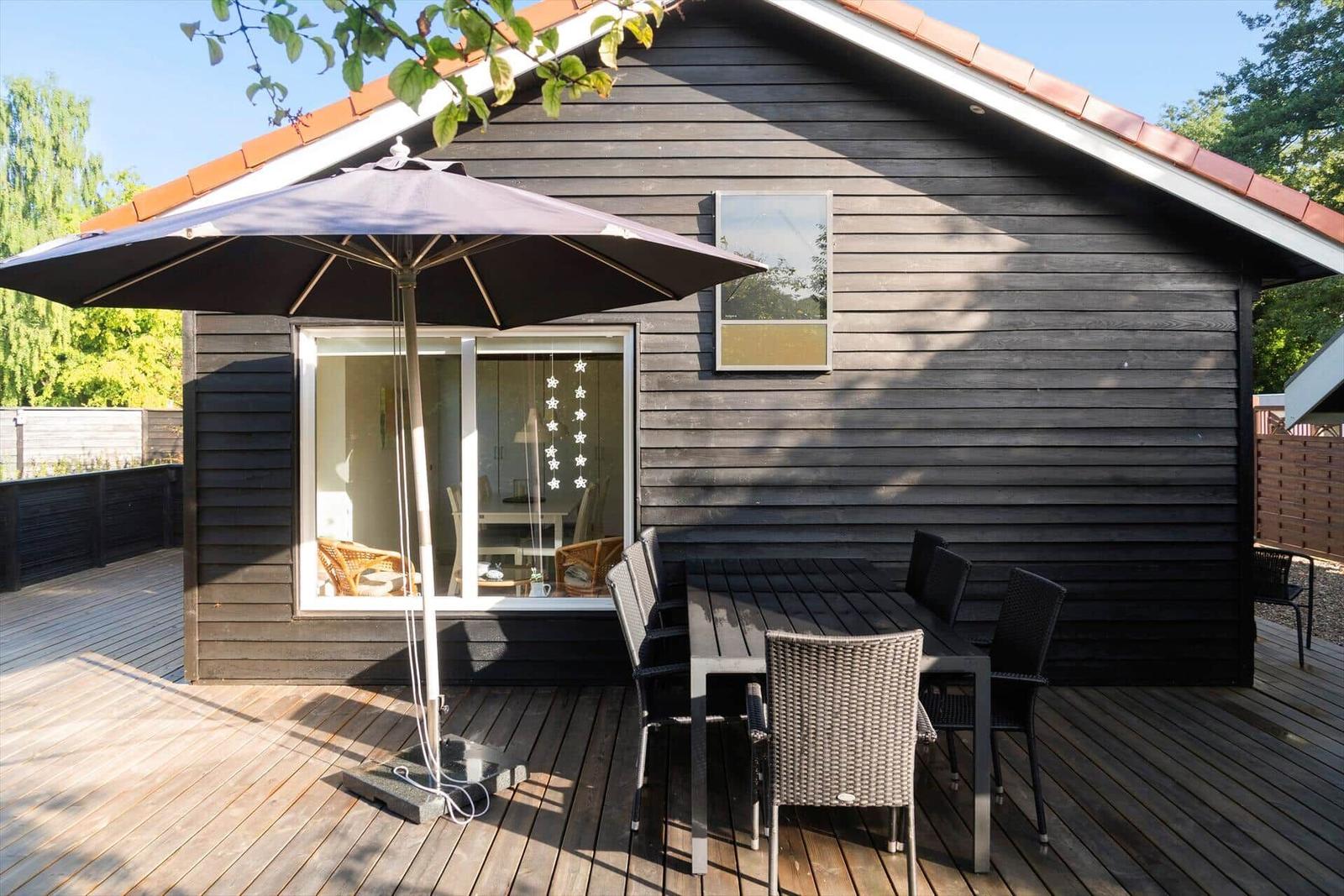 Deck with table, chairs, and umbrella in front of a wooden house.