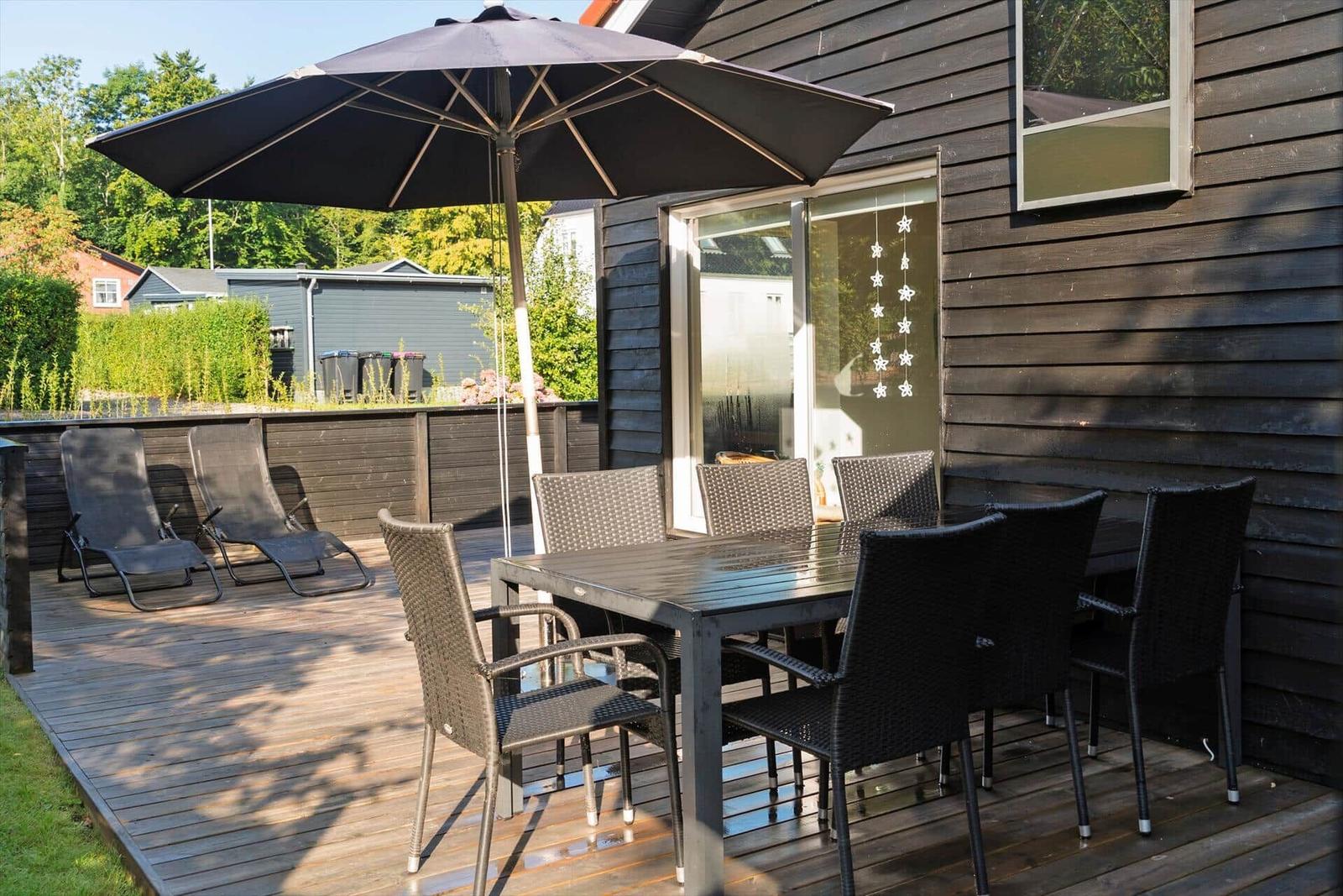 Deck with table, chairs, and umbrella next to house wall.