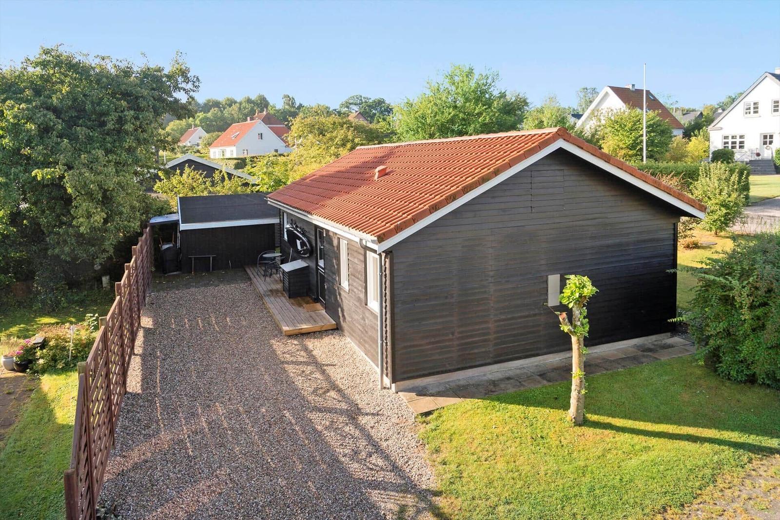 A dark wood-paneled house with a red roof and small wooden terrace.