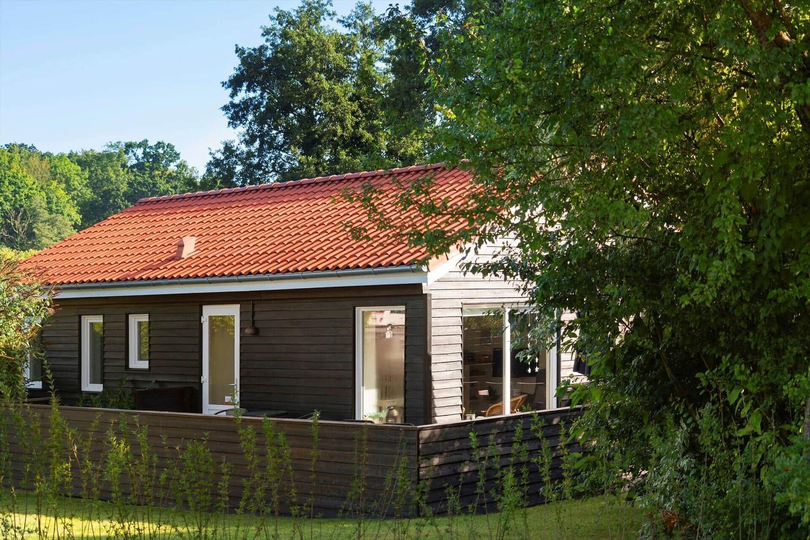 A house with a red roof and wooden siding, surrounded by trees and a garden.