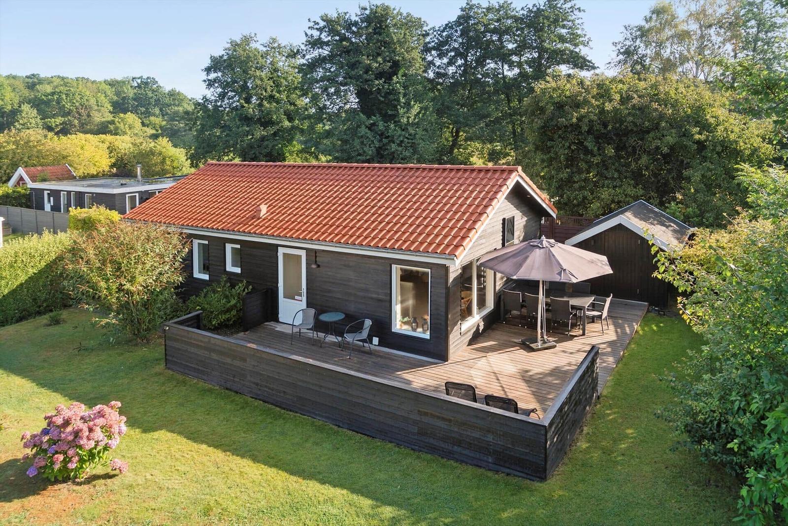 A house with terrace, garden, and umbrella. Surrounded by trees and greenery.