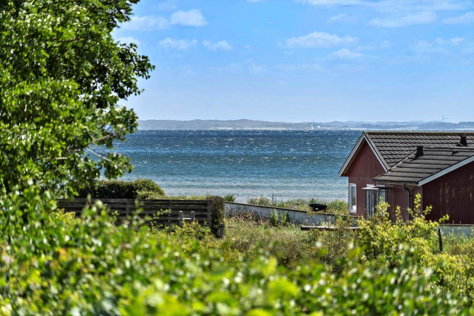 Red house with sea view and green vegetation in the foreground.