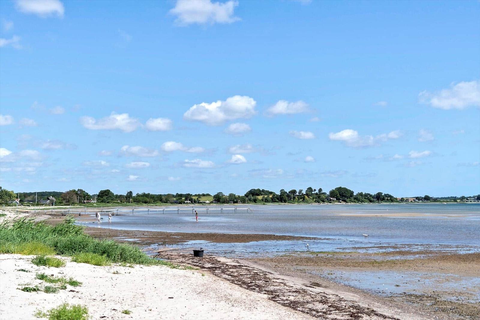 Beach with tidal flats, clear sky, and a few people in the water.