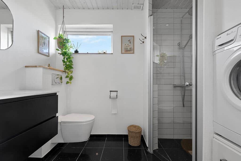 Badezimmer mit Dusche, Toilette und Waschmaschine. Schwarze Fliesen und weiße Wände.