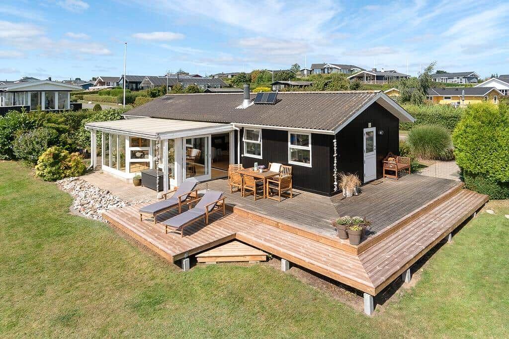 Schwarzes Haus mit Terrasse, Garten und Sonnenschutz. Holztische und Liegestühle.
