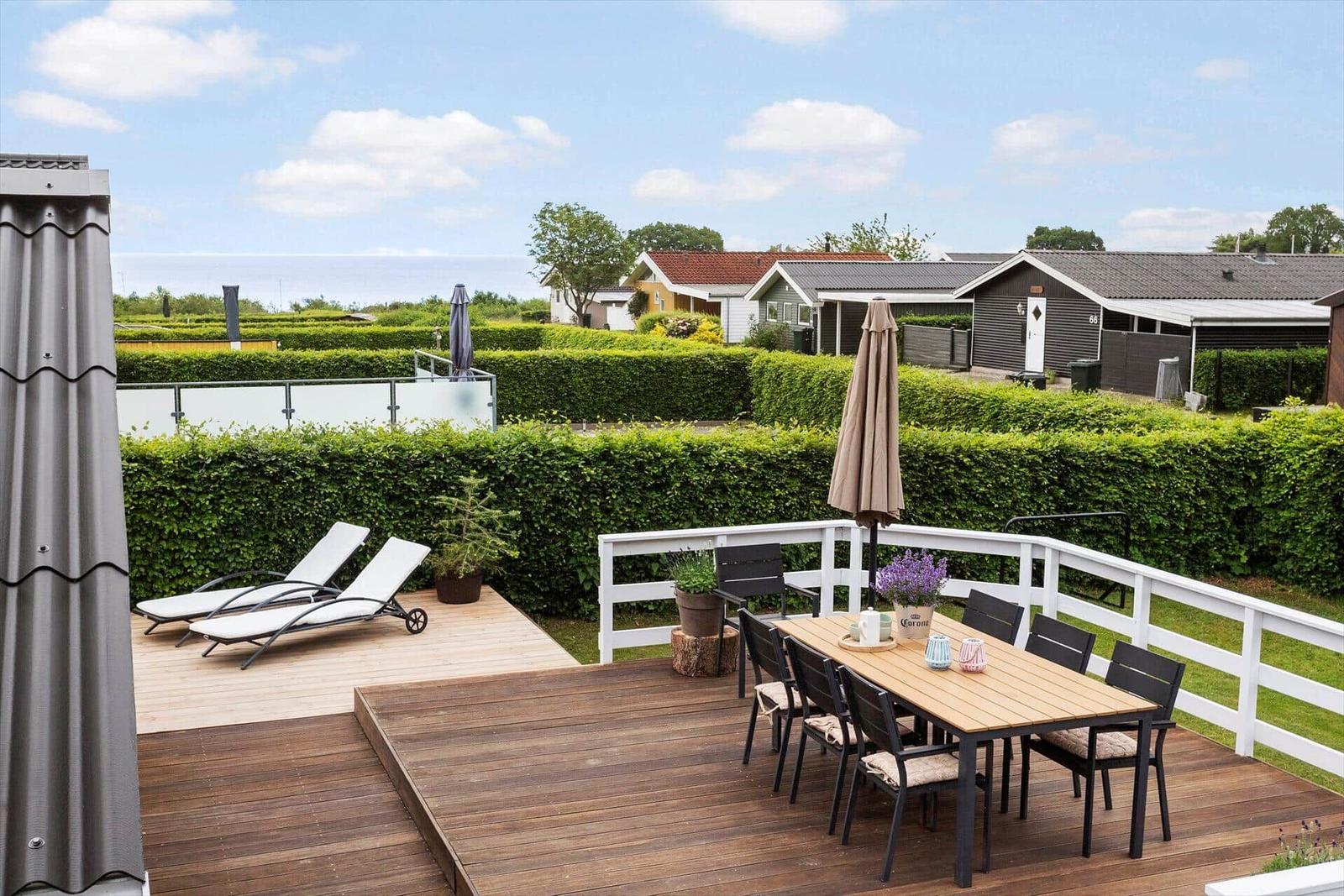 Terrasse mit Esstisch, Liegestühlen und Blick auf grüne Hecken und Ferienhäuser.