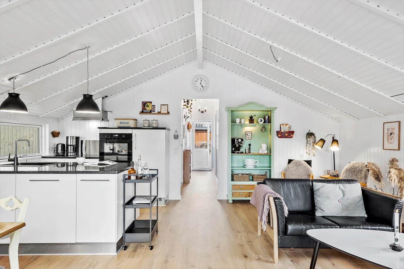 Küche mit Arbeitsplatz, Wohnbereich mit Sofa und Schrank. Holzboden und weißer Dachstuhl.