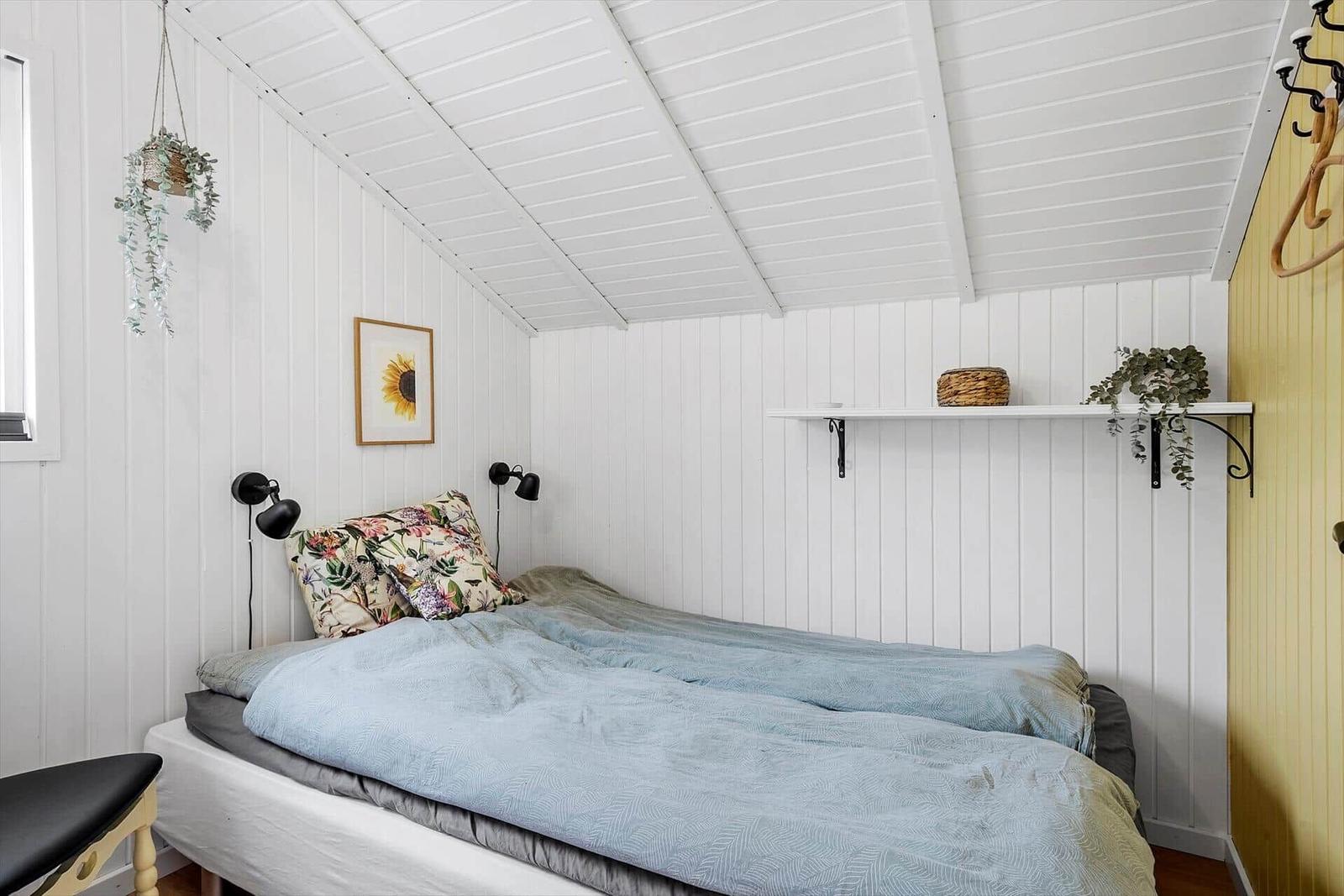 Schlafzimmer mit Bett, Wandregal und hängenden Pflanzen an weiß verputzten Wänden.