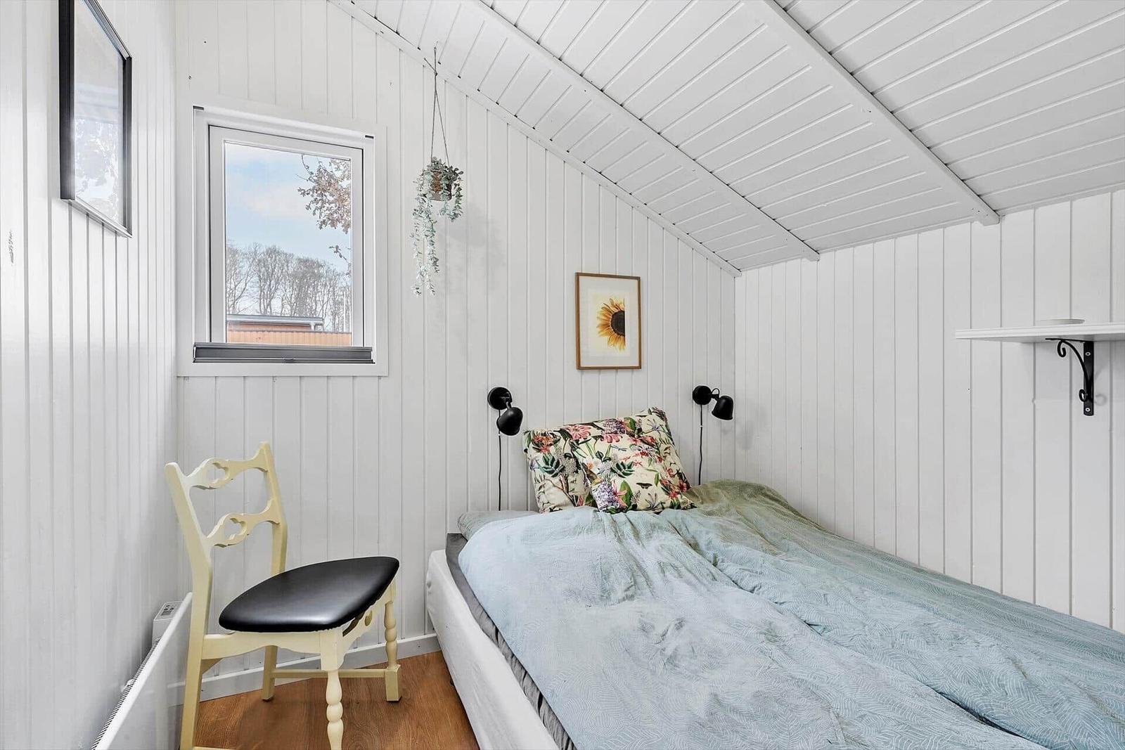 Schlafzimmer mit Bett, Stuhl und Fenster. Weiße Wände und Decke.