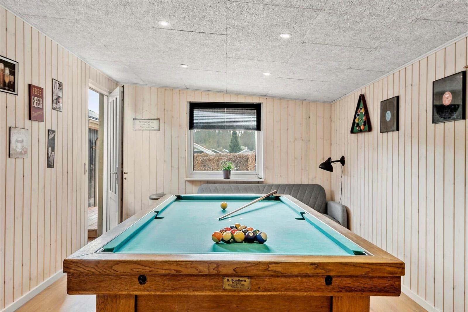 Pooltisch mit grünem Filz und Bällen in einem Raum mit Holzwandverkleidung und Fenster.