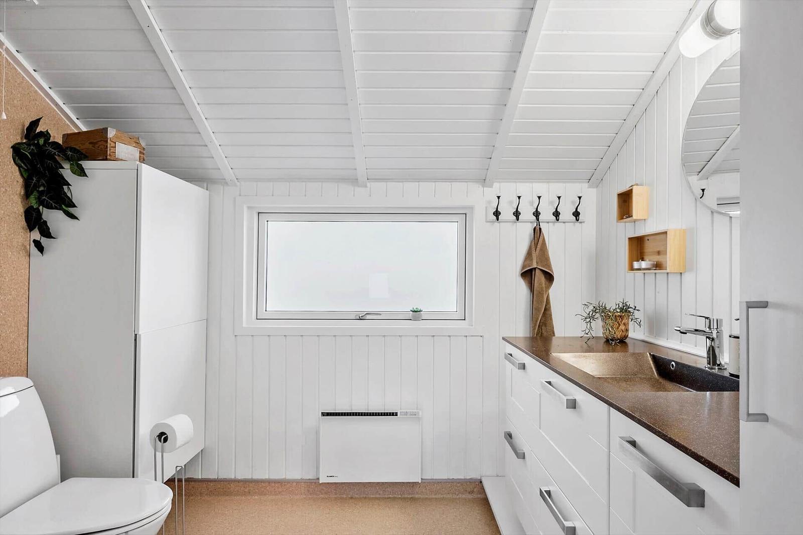 Badezimmer mit weißer Holzwand, Fenster, Waschbecken und Toilette.