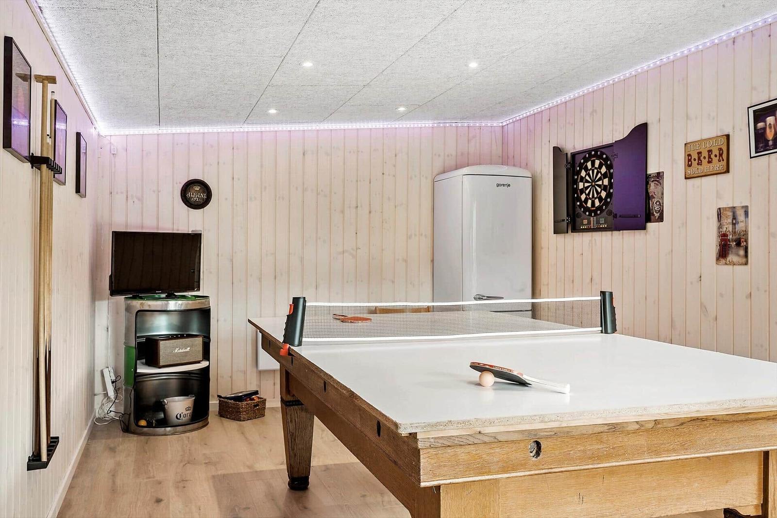 Raum mit Tischtennisplatte, Dartboard und Kühlschrank an Holzwänden.