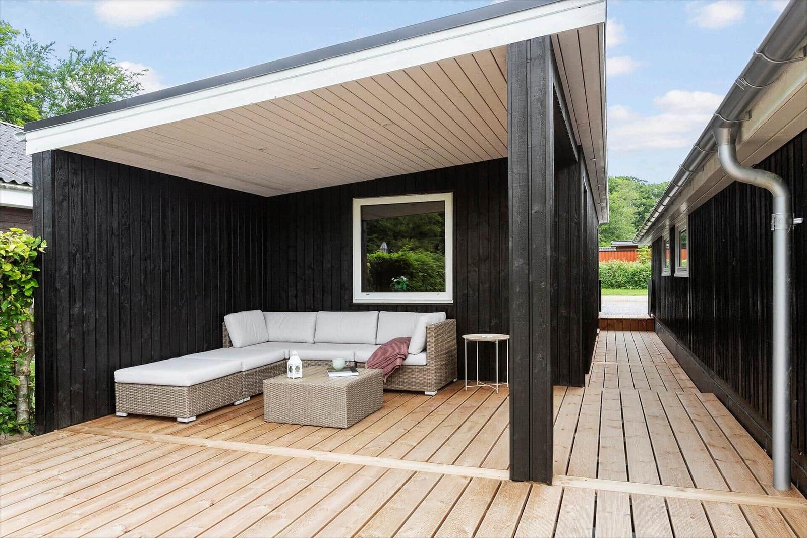 Terrasse mit Sitzgruppe unter Dach, Holzdecke und dunkler Fassade.