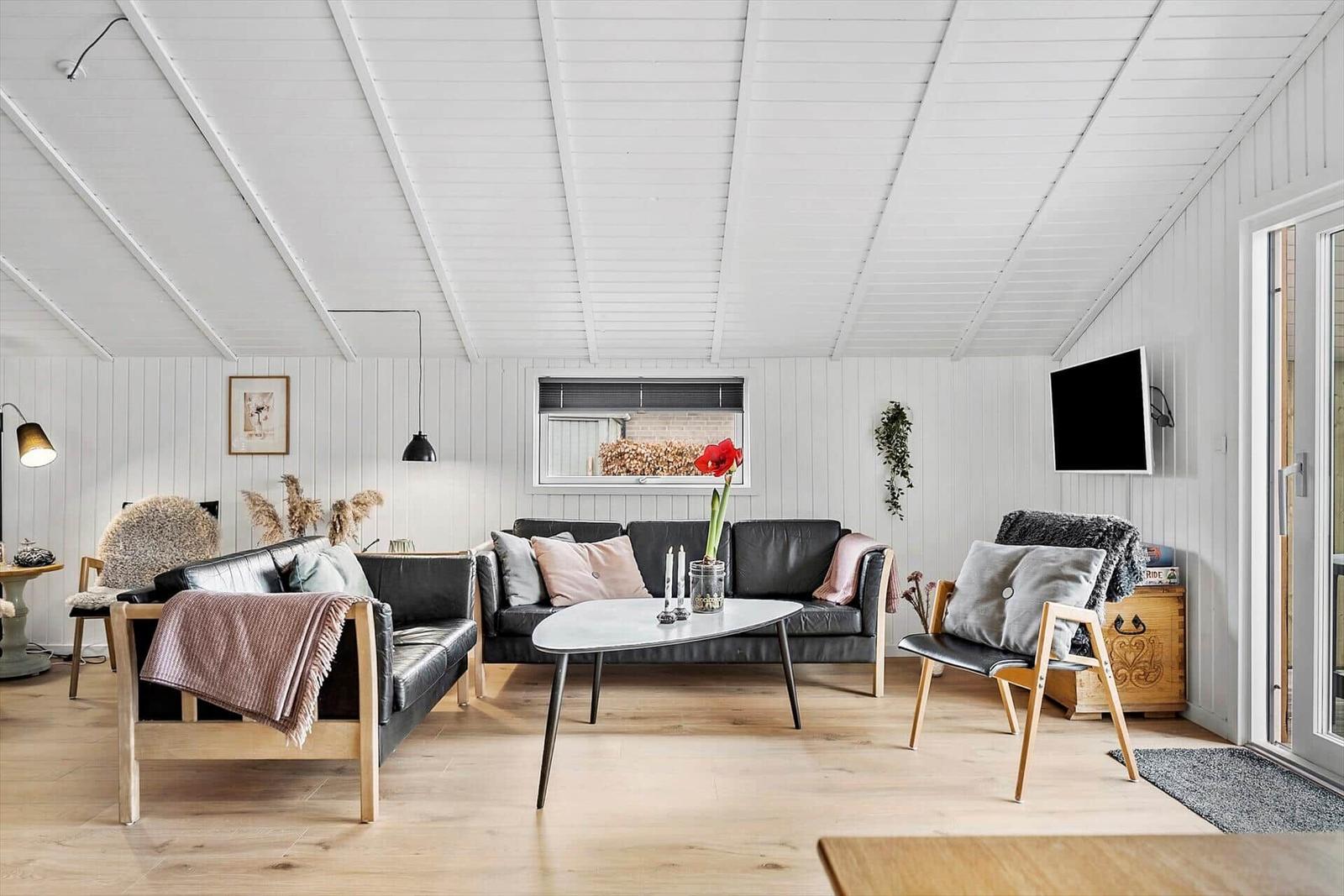 Wohnzimmer mit schwarzen Ledersofas, Holzmöbeln und weißer Holzwandverkleidung.