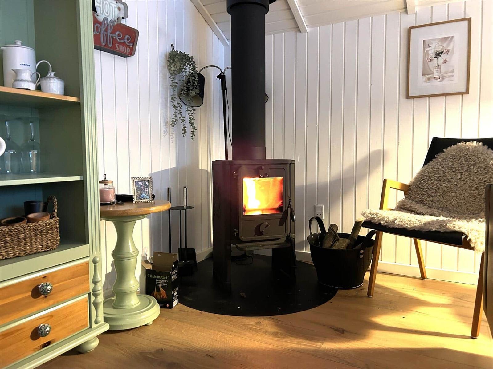 Raum mit Kaminofen, Holzfußboden, Stuhl mit Felldecke und grünem Schrank.