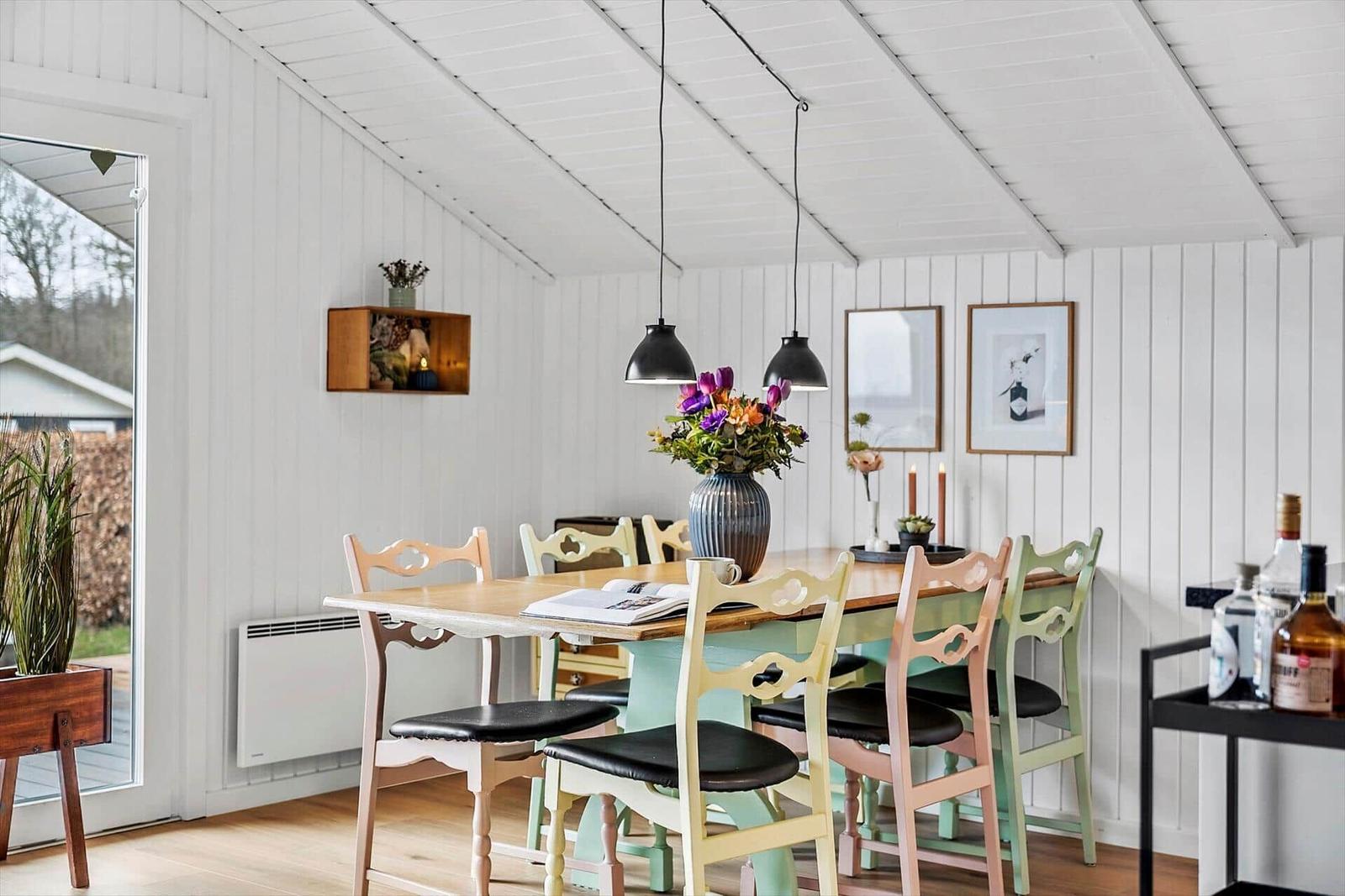 Esszimmer mit Holztisch, bunten Stühlen und Blumenvase unter Hängelampen.