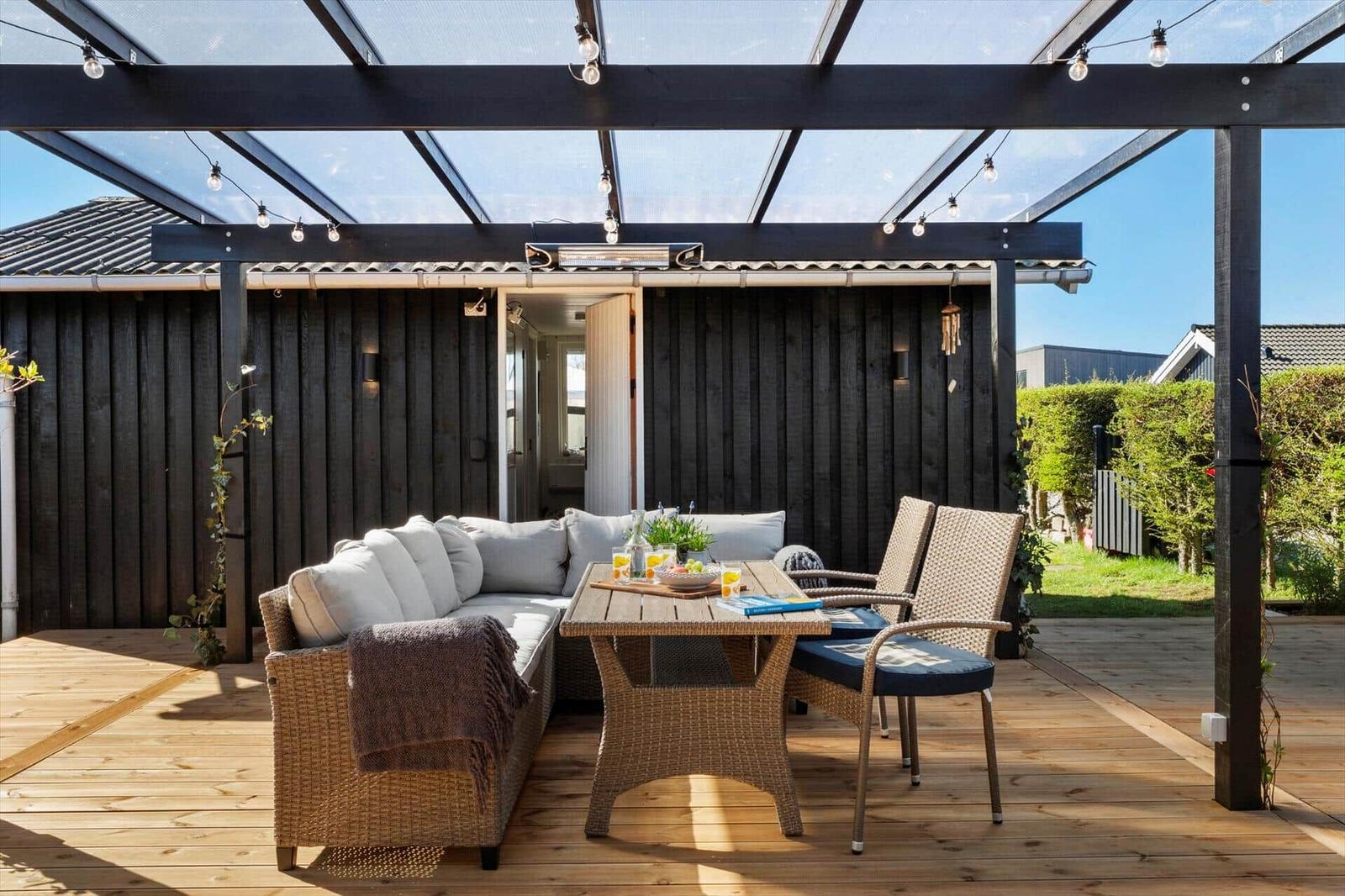 Terrasse mit Sitzgruppe, Tisch und Decke unter Glasdach mit Lichterkette.