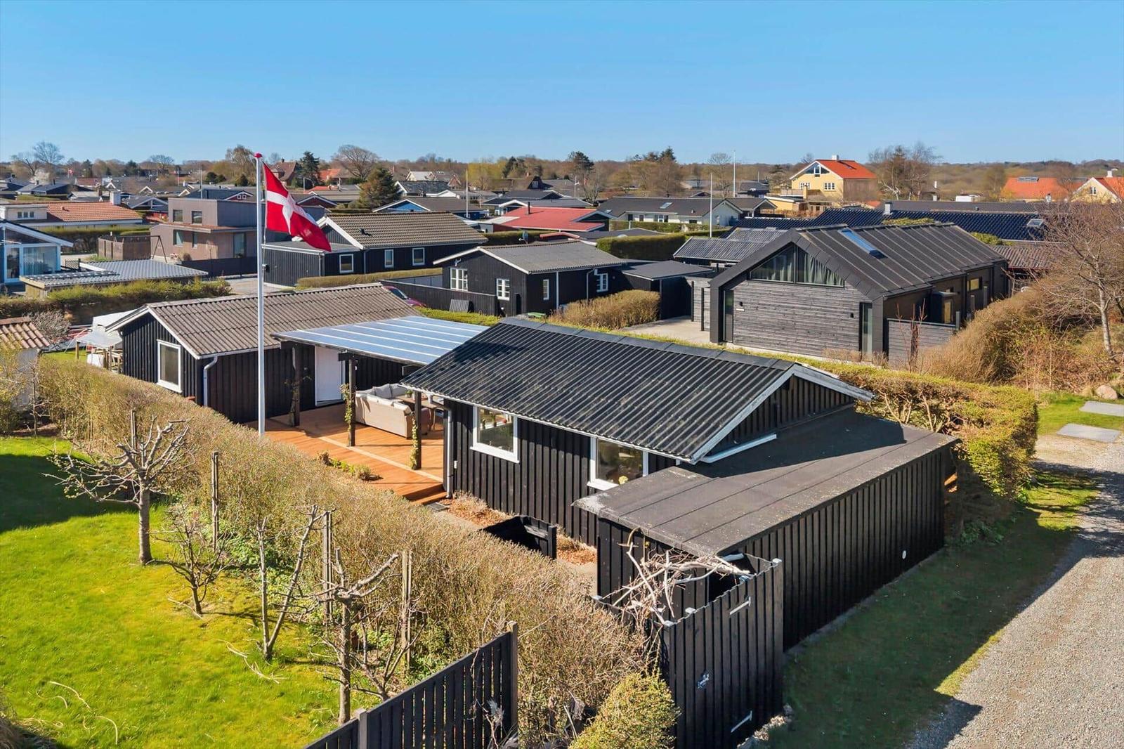 Schwarze Holzhäuser mit Garten und Flagge. Blick auf Wohngebiet mit Dächer und Bäumen.