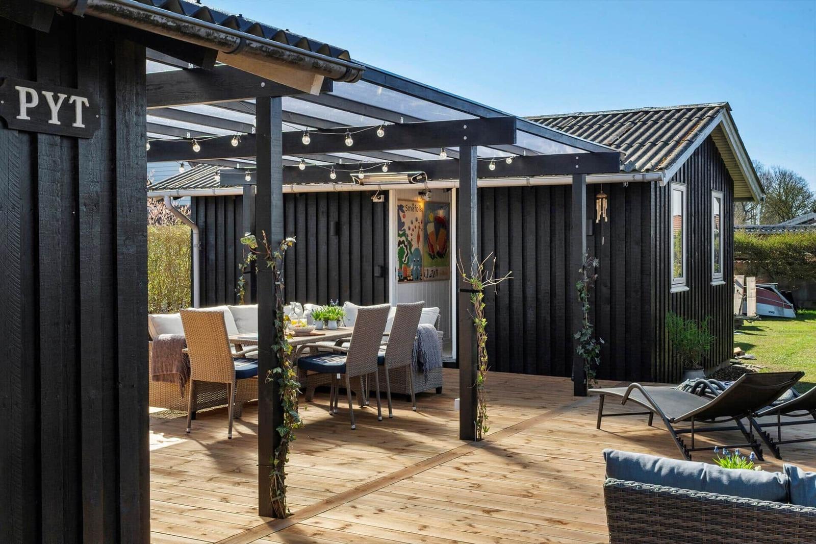 Terrasse mit Sitzgelegenheiten und Grillbereich. Schwarze Holzwand und Holzdecke.