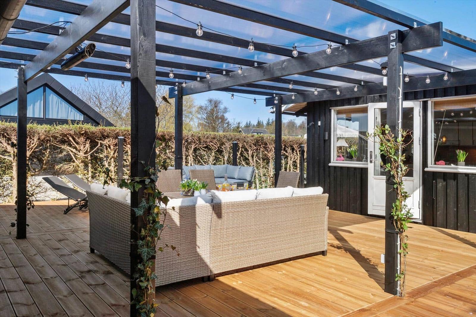 Terrasse mit Sitzgruppe unter Dach, Holzboden und Lichterkette.