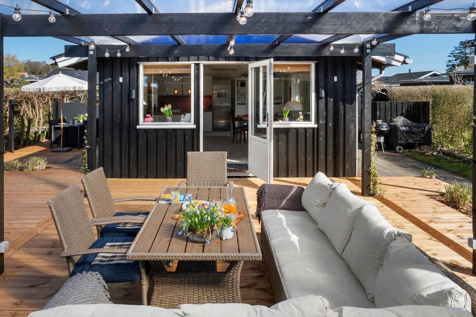 Terrasse mit Sitzgruppe, Tisch und Grill unter einem Dach.