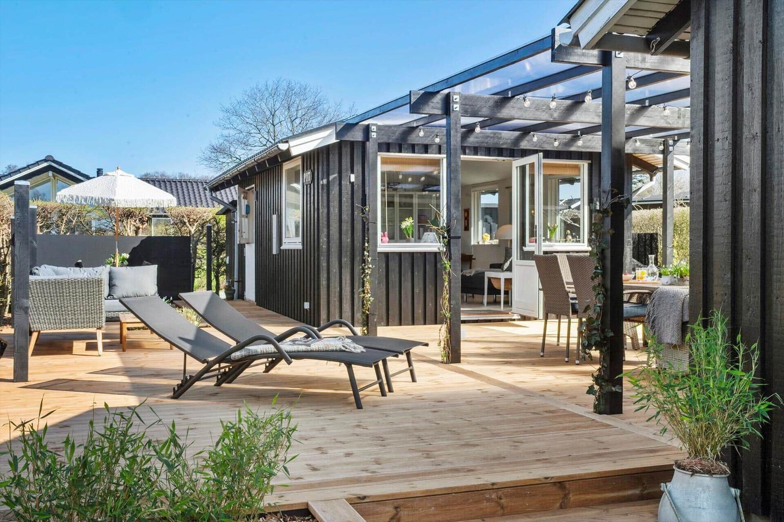 Terrasse mit Liegen, Sitzgruppe und Überdachung. Haus mit Fenstern und offener Tür.
