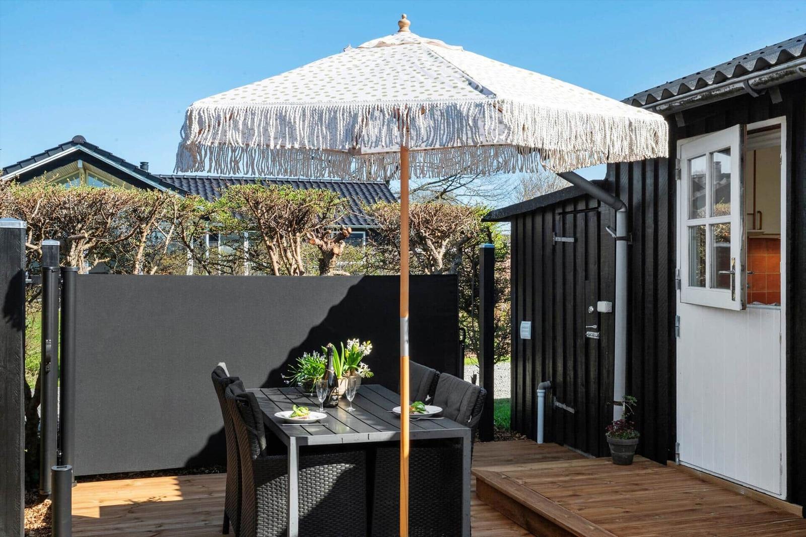 Terrasse mit Tisch, Stühlen und Sonnenschirm. Tür führt ins Haus.