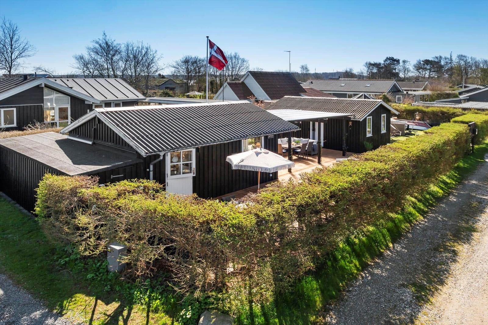 Moderne Holzhütte mit Terrasse, Garten und dänischer Flagge.