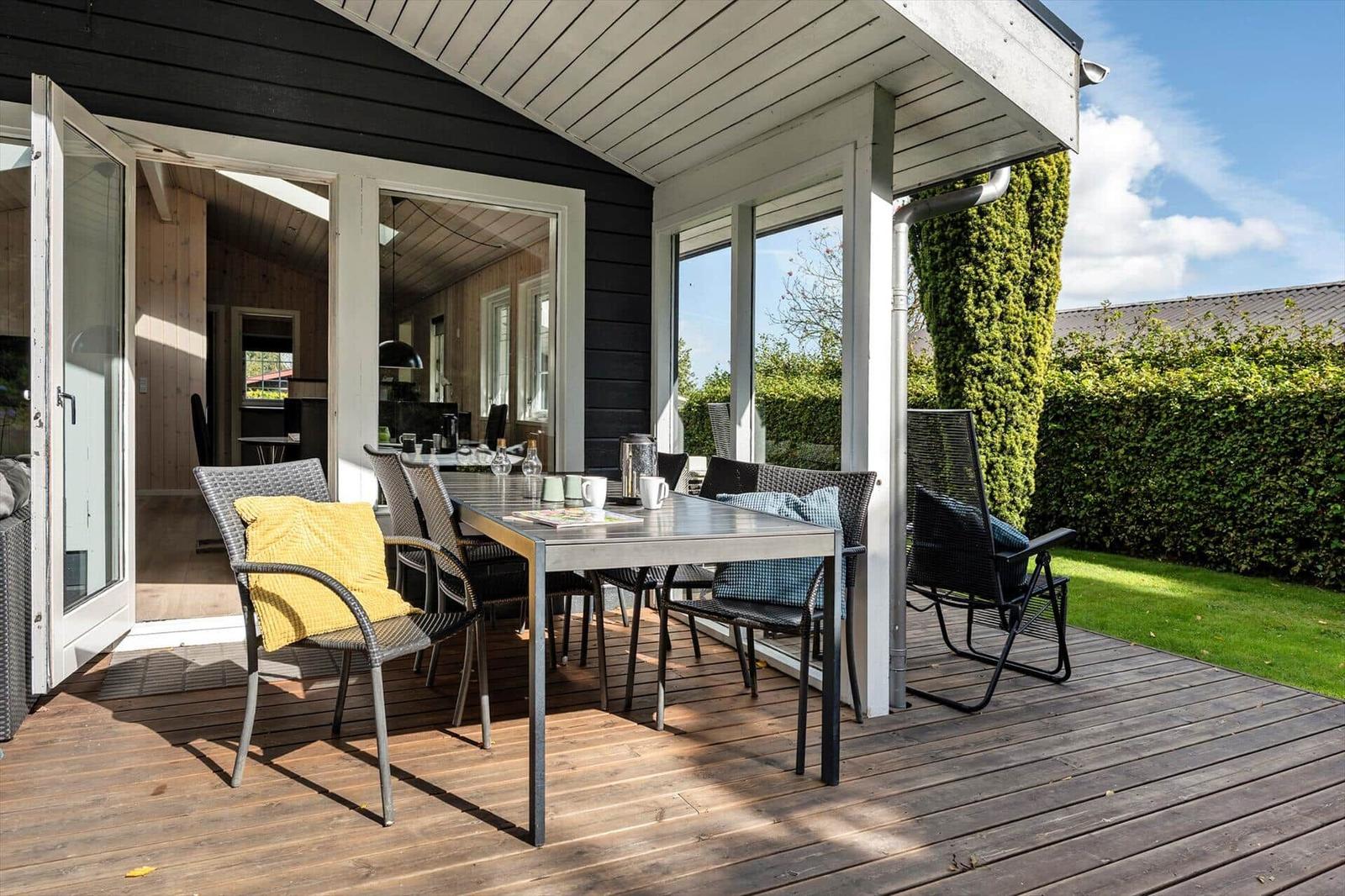 Terrasse mit Tisch und Stühlen, Blick in das Haus, grüner Garten im Hintergrund.