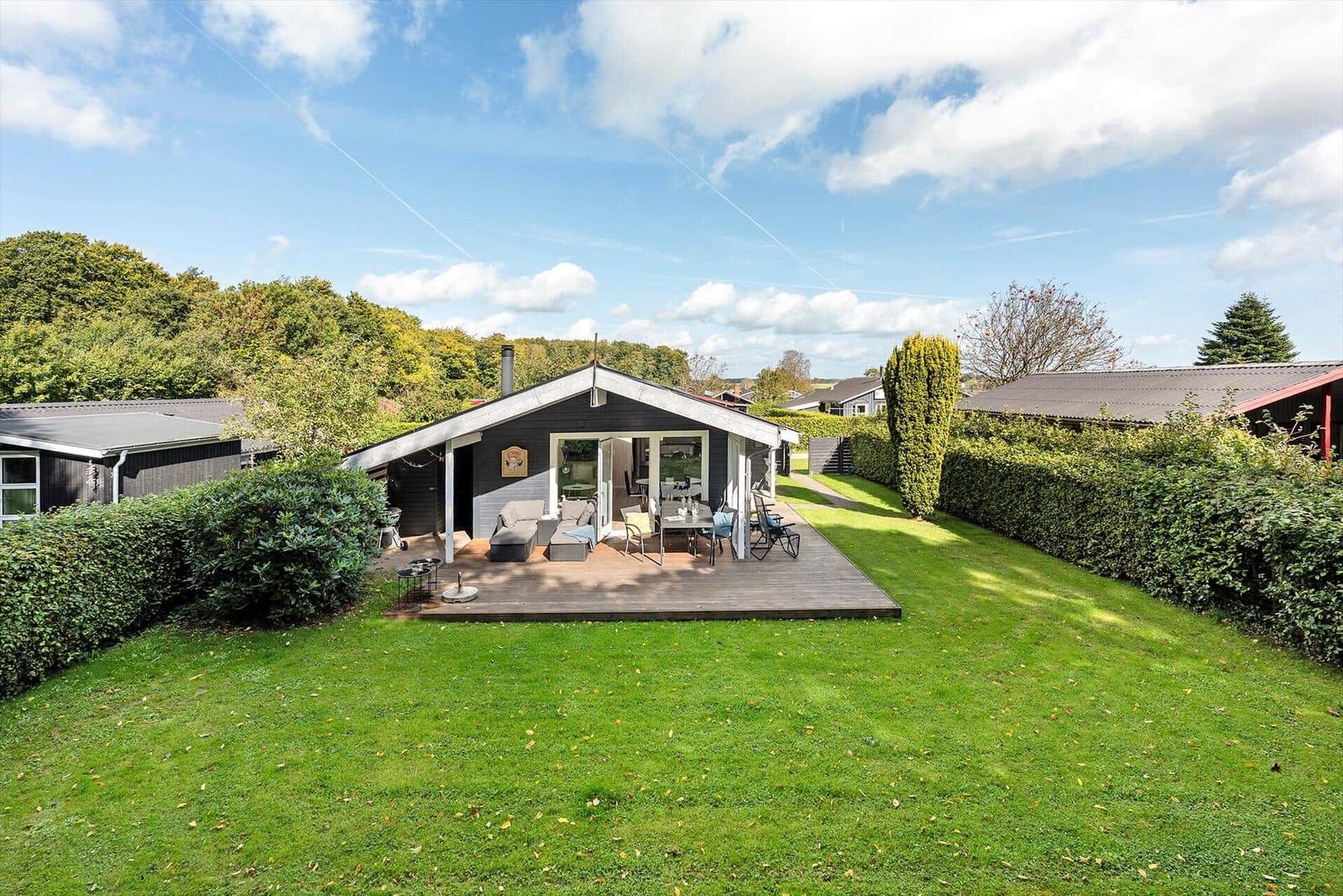 Haus mit Terrasse, Garten und Grillplatz unter blauem Himmel.