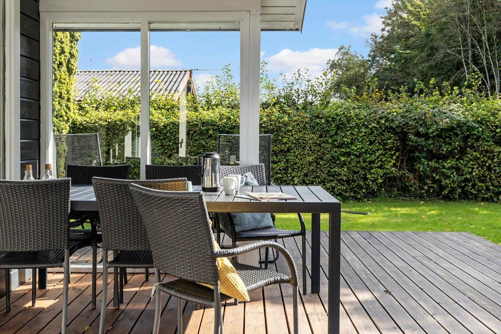 Terrasse mit Tisch und Stühlen, Blick auf grünen Garten und Himmel.