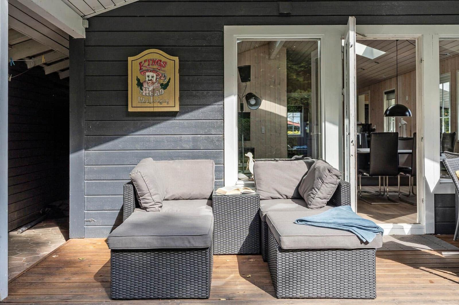 Terrasse mit zwei Sitzgruppen und Blick ins Haus. Wand mit Schild.
