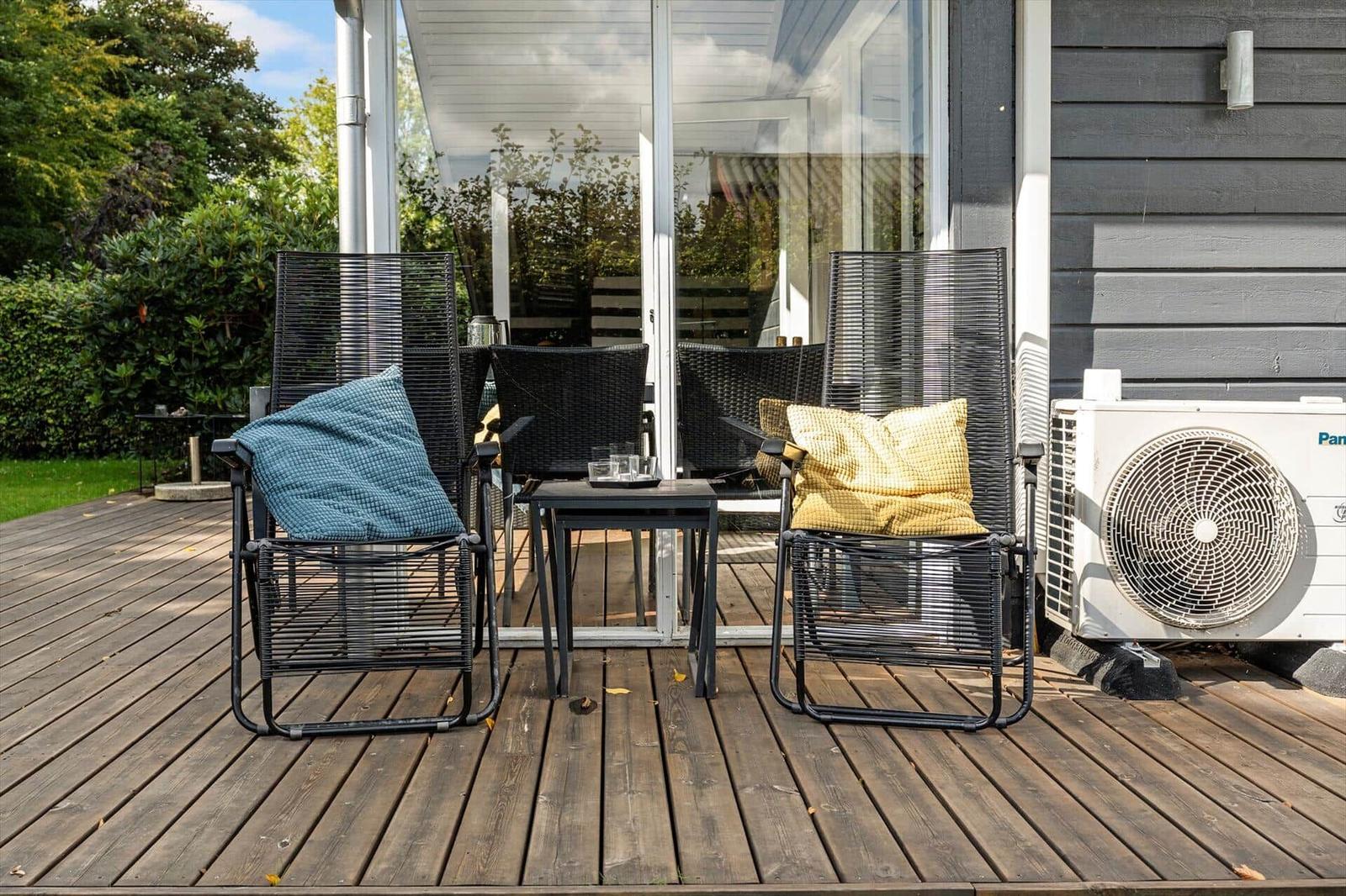 Terrasse mit zwei Stühlen, Tisch und Kissen. Hintergrund: Haus und Grünfläche.