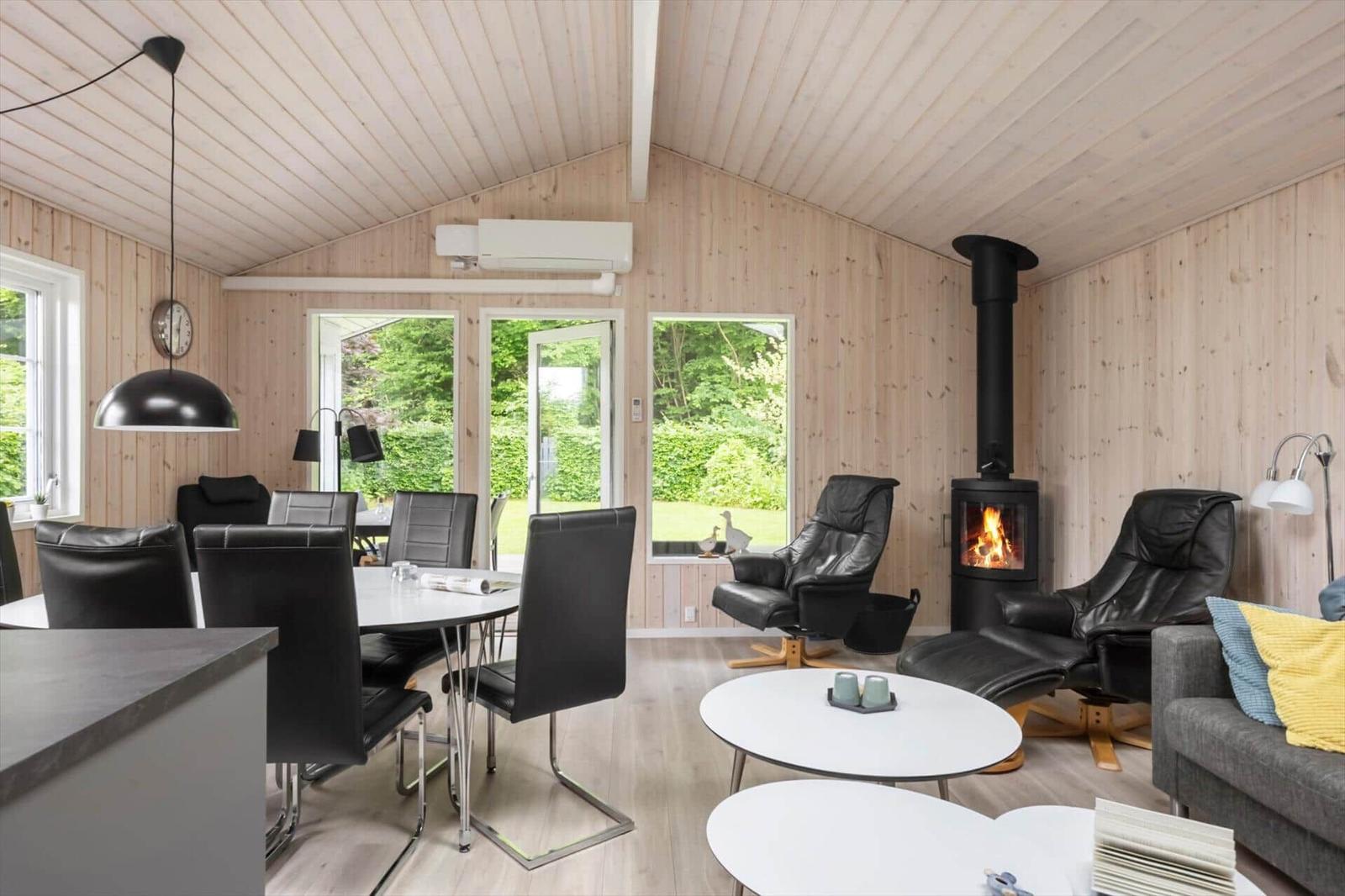 Wohn- und Essbereich mit Holzwand, Kamin und schwarzen Ledersitzen.