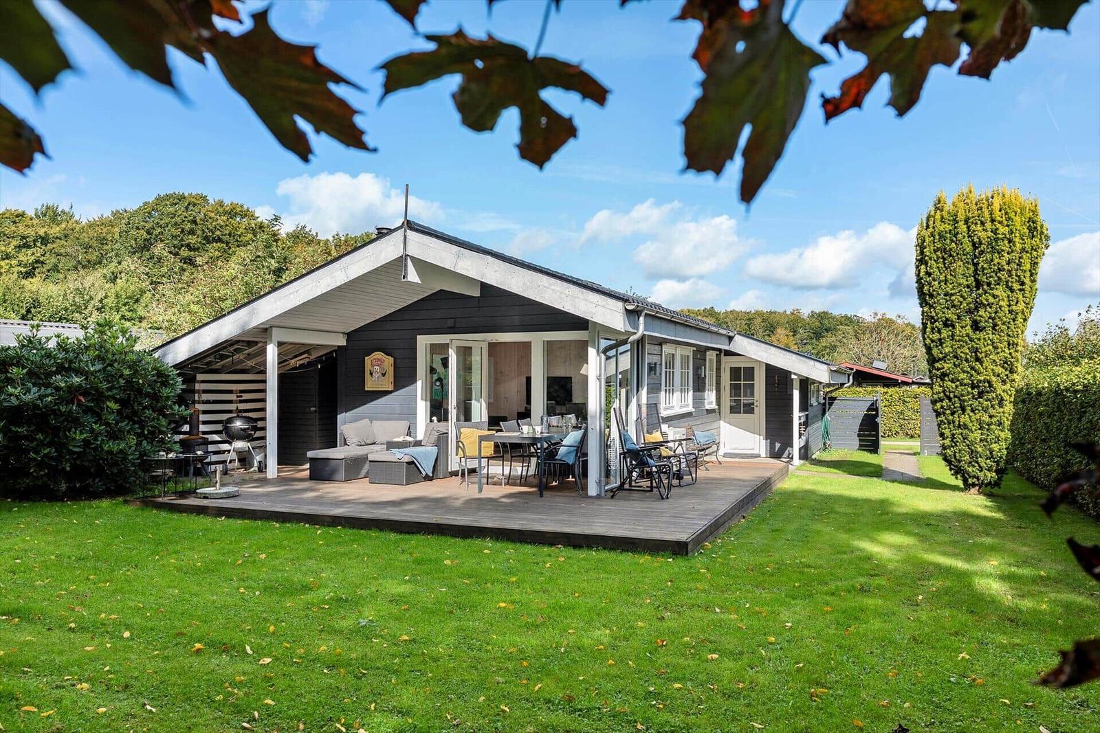 Moderne Villa mit Terrasse, Garten und Grillplatz unter blauem Himmel.