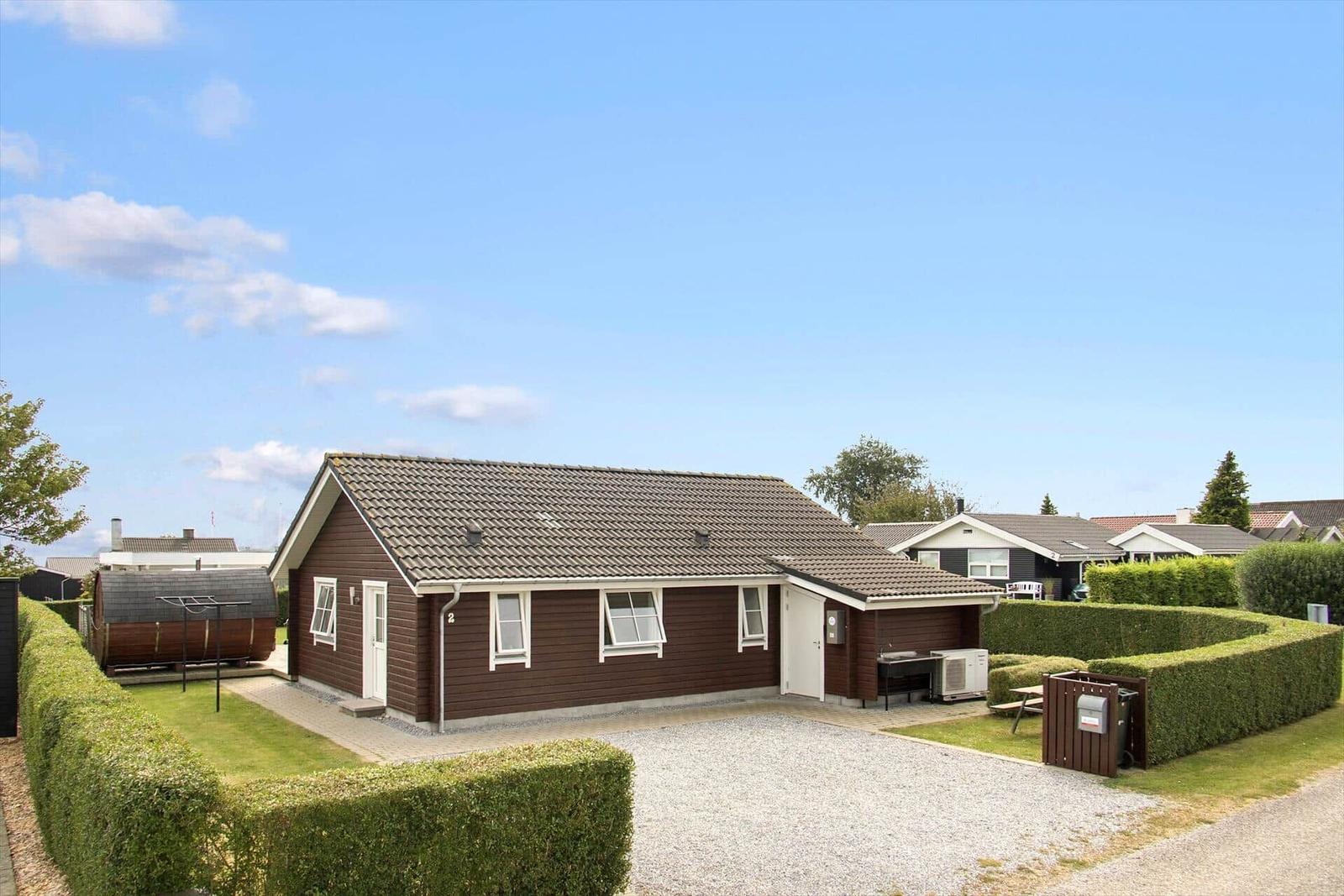 Ein braunes Ferienhaus mit weißer Tür und Fensterrahmen, umgeben von Rasen und Hecken.