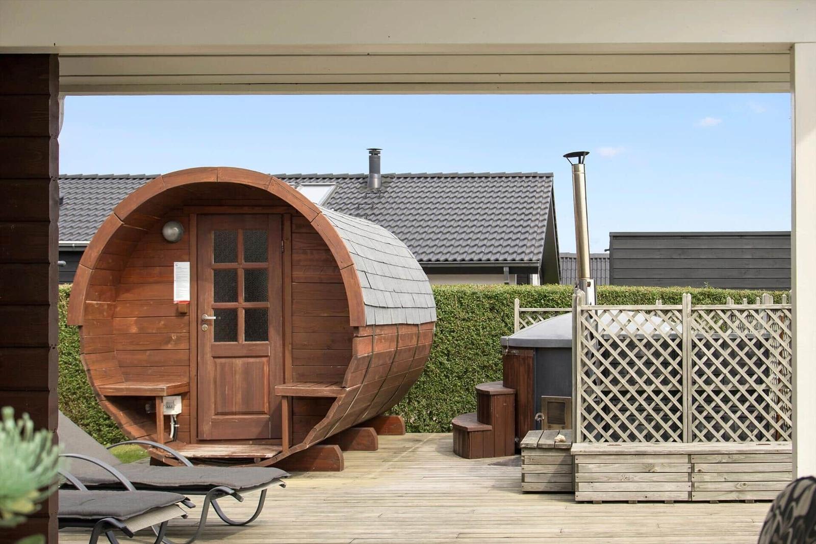 Holzsauna im Kegelförmigen Design auf Terrasse mit Liegestühlen und Hinterhofzaun.