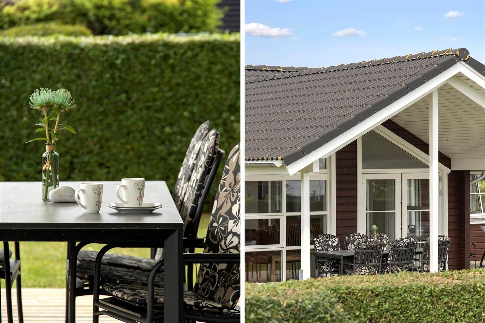 Terrasse mit Tisch, Stühlen und Blumen vor einem Haus mit Dach und Fenstern.
