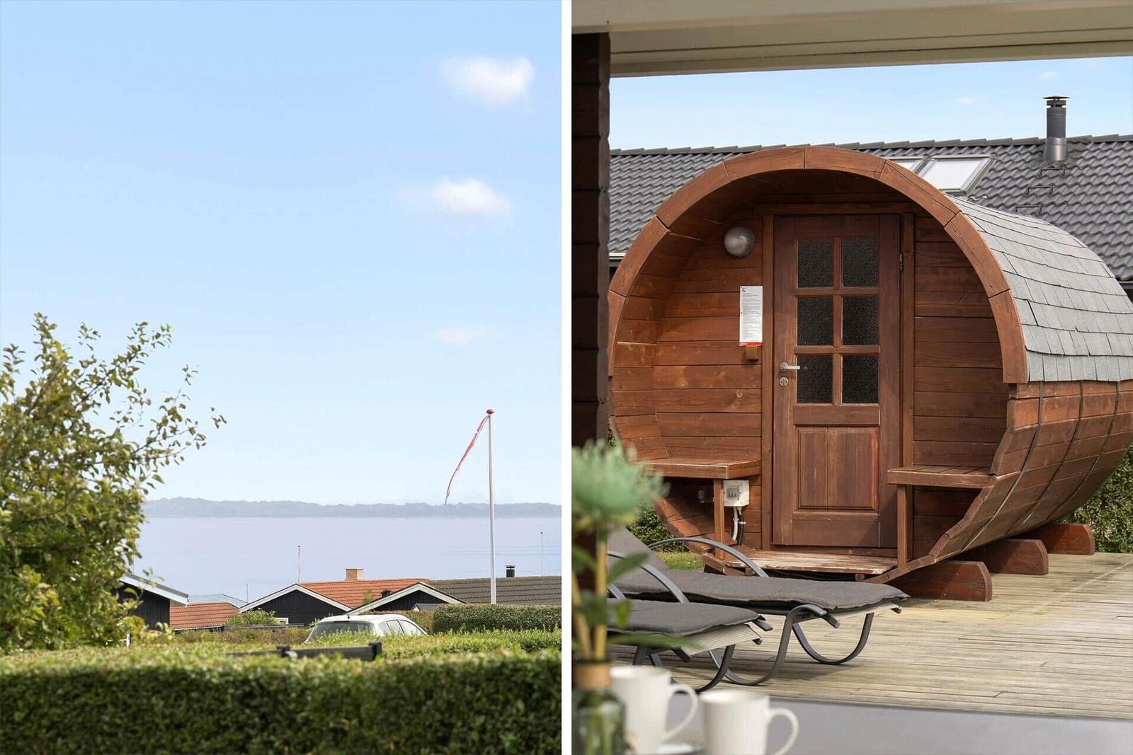 Holzsauna im Stil eines Fasses auf Terrasse mit Liegestühlen und Blick auf Wasser.
