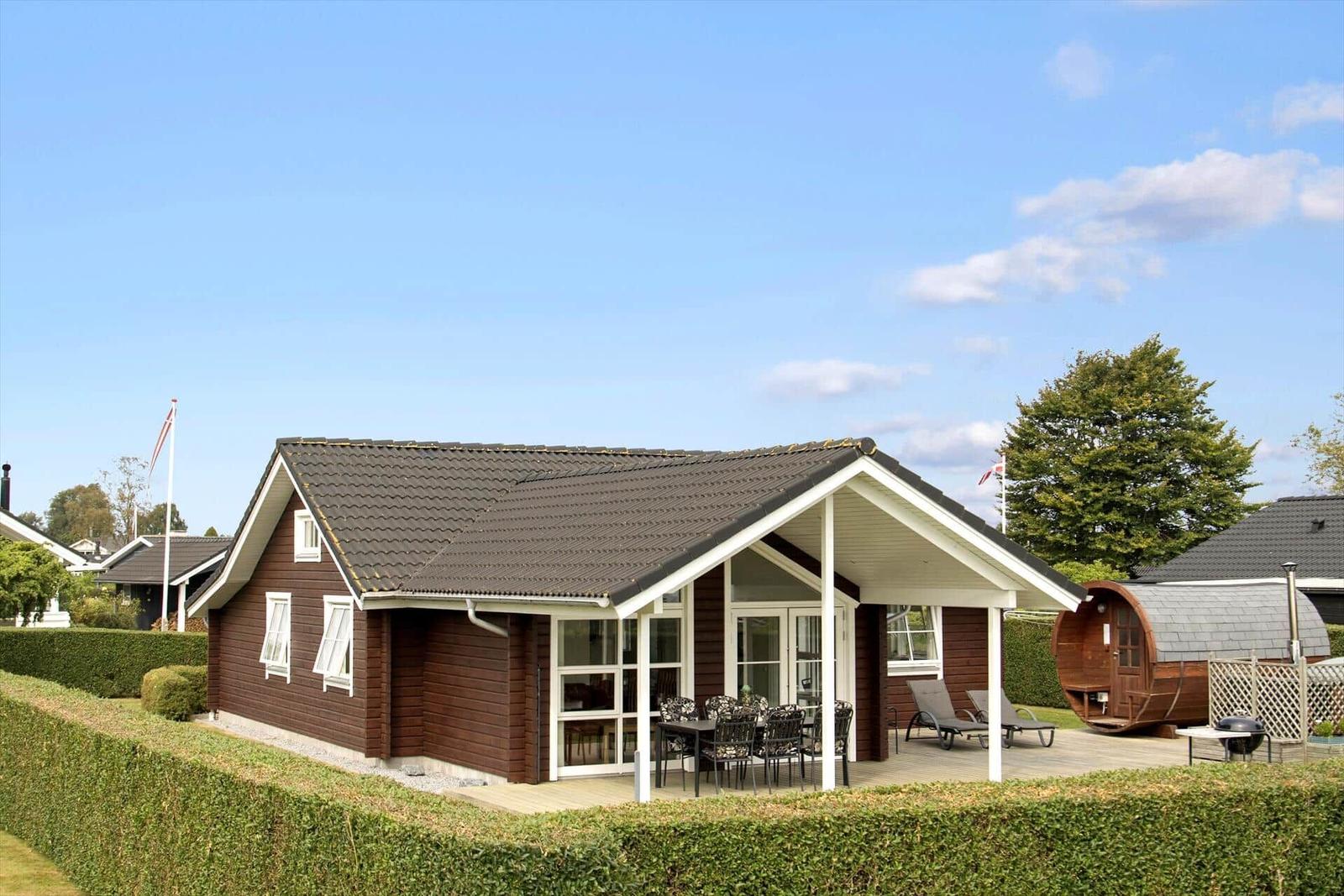 Ein Holzhaus mit Terrasse, Gartenmöbeln und einer Sauna im Hintergrund.