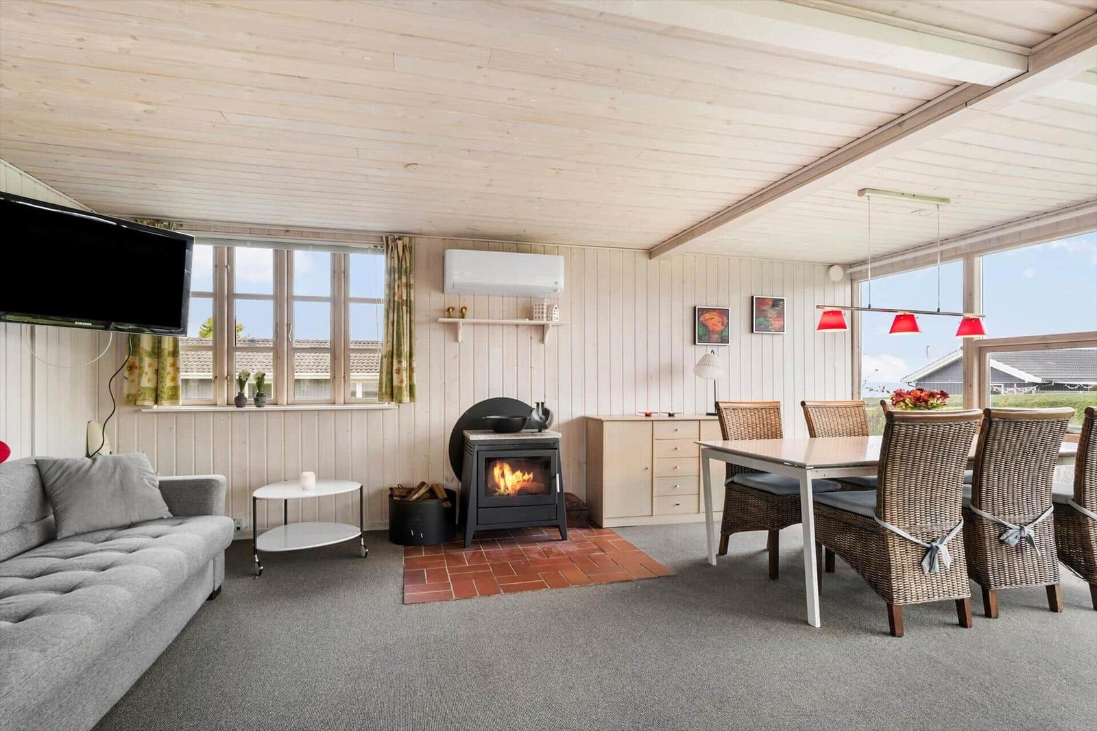 Wohn- und Essbereich mit Kamin, TV und Essgruppe. Holzwände und große Fenster.
