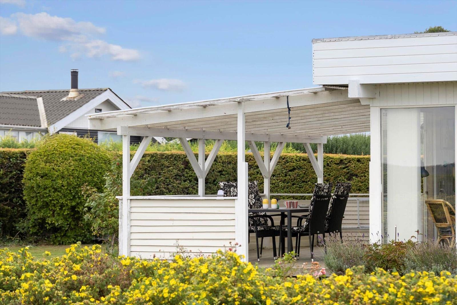 Terrasse mit Tisch und Stühlen unter einem weißen Vordach. Gelbe Blumen im Vordergrund.